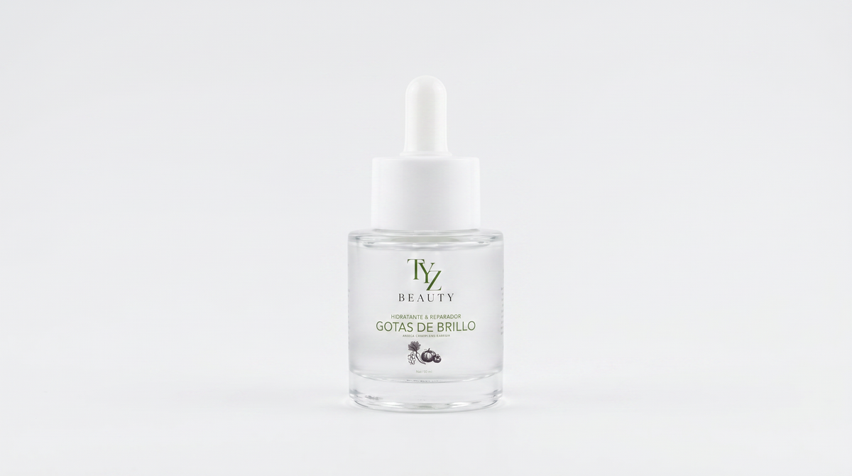 A clear glass dropper bottle with a white cap and white label, containing a transparent liquid. The label features the brand name 'TYZ BEAUTY' and the text 'GOTAS DE BRILLO' in green and gold, set against a seamless white background.